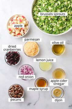 the ingredients for apple salad laid out in bowls on a white marble counter top, including apples, parmesan cheese, cranberries, olives, lemon juice and maple syrup
