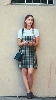a woman standing in front of a wall looking at her cell phone and holding a purse
