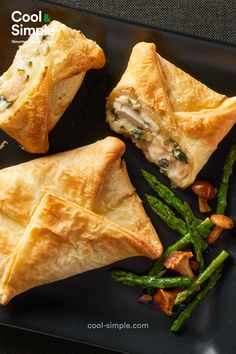 two pastries on a black plate with asparagus and other food items next to it