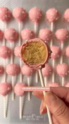 a hand holding a pink lollipop in front of a wall of candy balls