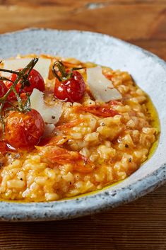 a white bowl filled with rice and tomatoes on top of a wooden table next to a fork