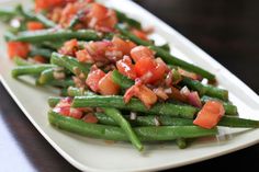a white plate topped with green beans covered in tomatoes and onion topping on top of it