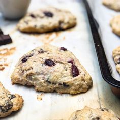 cookies with cranberries and chocolate chips are on a baking sheet next to a bowl of cherries
