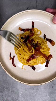 a person is holding a fork over a plate of spaghetti with bacon on it,