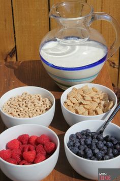 four bowls with cereal, berries and yogurt in front of a pitcher of milk