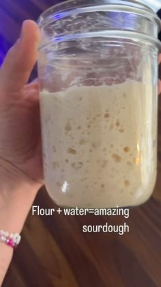 a person holding a jar with some liquid in it and the text flour + water - amazing sourdough