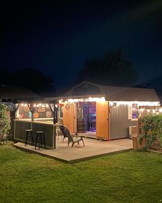 an outdoor bar with lights on the roof and two stools in front of it