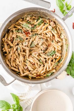 a pan filled with pasta and spinach on top of a white table next to silver utensils
