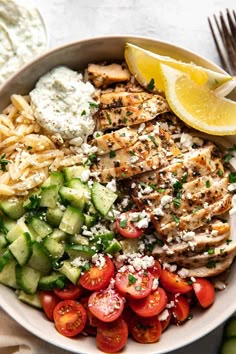 a white bowl filled with chicken, cucumber, tomatoes and feta cheese