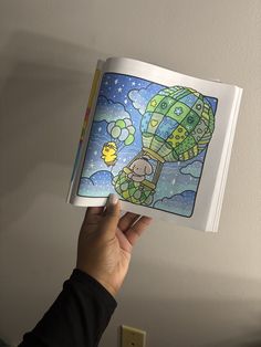 a person holding up a coloring book with an image of a hot air balloon in the sky