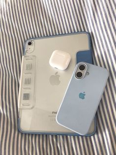 two iphones sitting on top of a bed next to an airpods charger