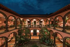 an indoor courtyard at night with lights on and plants growing in the arches around it