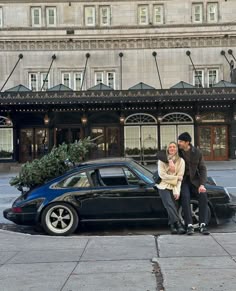 a man and woman sitting on top of a black car