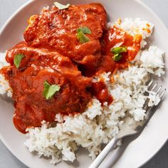 two pieces of meat covered in sauce and rice on a white plate with a fork