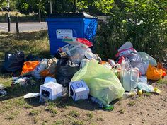 a pile of garbage sitting on the side of a road next to a blue trash can