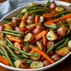 a bowl filled with potatoes, green beans and carrots on top of a wooden table