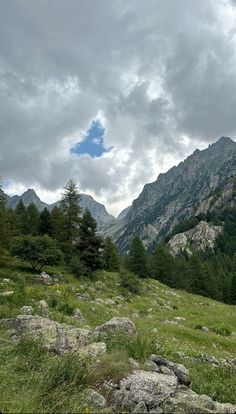 the mountains are covered in green grass and some rocks with trees on them under a cloudy sky