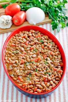 a red bowl filled with beans and veggies on top of a striped table cloth