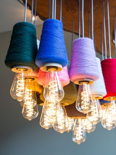 several spools of thread are hanging from a chandelier with light bulbs