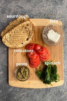 a cutting board with bread, tomatoes, spinach and other ingredients on it to make a sandwich