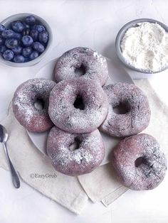 powdered doughnuts and blueberries are on a napkin next to bowls of berries