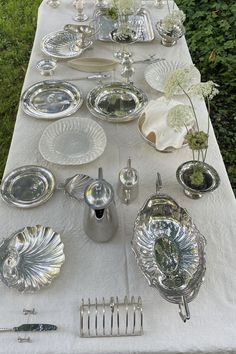 an outdoor table set with silver dishes and flowers