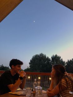 two people sitting at a table with wine glasses in front of them and the sky behind them