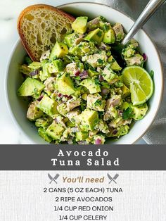 a salad with avocado and tuna is in a white bowl next to a slice of bread