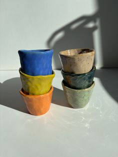four different colored bowls sitting next to each other on a white counter top with shadows from the wall behind them