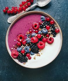 a bowl filled with berries and granola on top of a blue surface next to a spoon