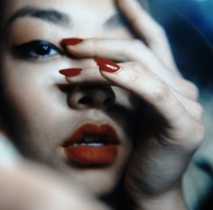 a woman with red nail polish holding her hand to her face