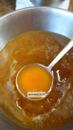 a ladle full of orange liquid in a metal bowl on a counter top next to a white napkin