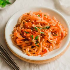 a white plate topped with noodles and carrots next to chopsticks on a table