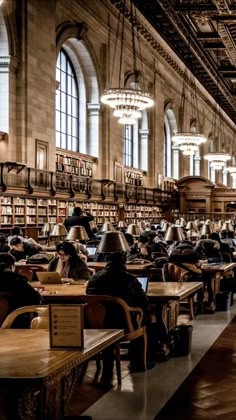 people sitting at desks in a large room with lots of bookshelves and chandeliers