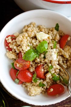 a white bowl filled with rice, tomatoes and spinach leaves next to a fork