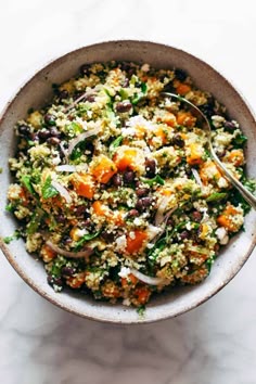 a bowl filled with rice and vegetables on top of a white countertop next to a spoon
