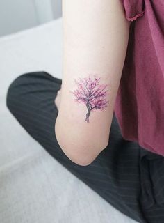 a woman's arm with a small pink tree tattoo on the left side of her arm