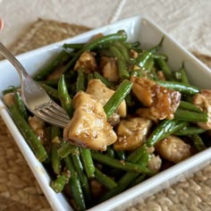 a person is holding a fork over a bowl of green beans with chicken and mushrooms