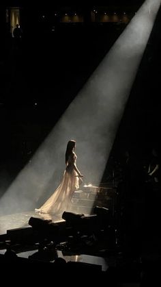 a woman in a white dress standing on stage with light streaming through her head and hands behind her back