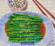 green beans with sesame seeds in a blue and white bowl next to chopsticks
