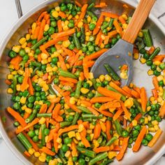 peas, corn and carrots in a pan with a wooden spoon on the side