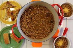 a pot filled with beans next to two plates of food on a tablecloth covered floor