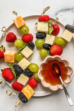 fruit and cheese skewers are arranged on a plate with a bowl of honey
