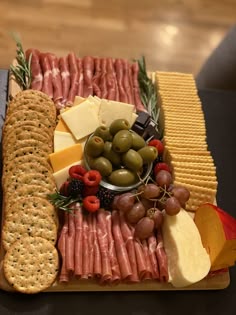 an assortment of cheeses, crackers and olives on a platter with meat
