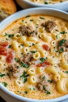 two bowls filled with pasta and meat soup on top of a table next to bread