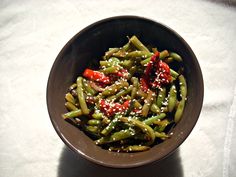 a brown bowl filled with green beans covered in sesame seeds and seasoning sprinkles