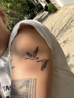 a person with a bird tattoo on their arm next to a building and trees in the background