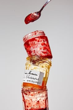 a spoon is pouring honey into jars filled with jams and other things to eat