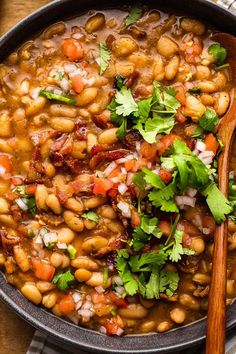 a bowl filled with beans and cilantro on top of a wooden table next to a spoon