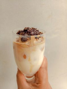 a hand holding a glass filled with ice cream and toppings
